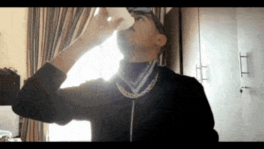 a man wearing sunglasses and a gold chain drinks from a white cup