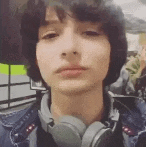 a young man wearing headphones and a denim jacket is taking a selfie .