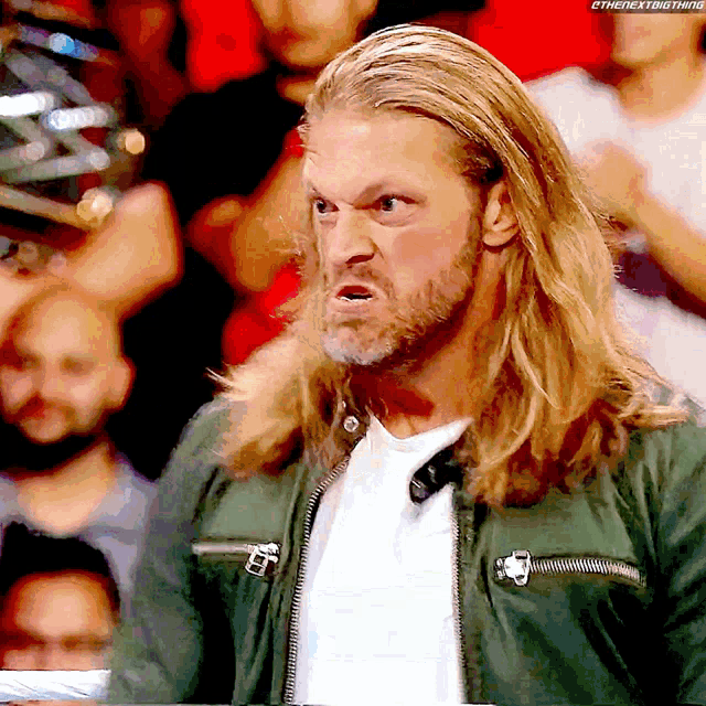 a man with long blonde hair and a beard is wearing a green jacket and white shirt