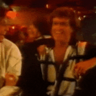 a man is smiling while sitting in a crowd of people in a bar .