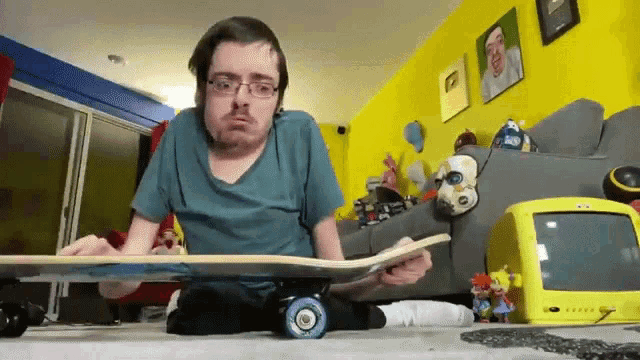 a man sitting on the floor holding a skateboard with a yellow tv behind him