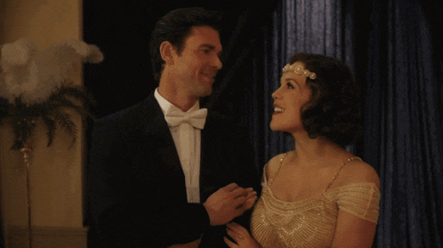 a man in a suit and bow tie stands next to a woman in a dress