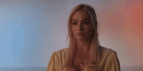 a blonde woman wearing a yellow shirt and a necklace is looking at the camera .