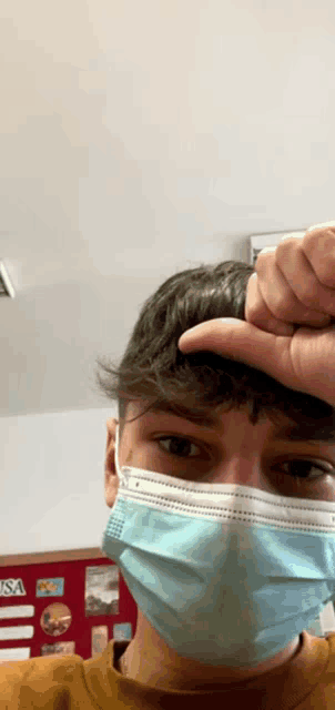 a man wearing a face mask holds his hand to his head