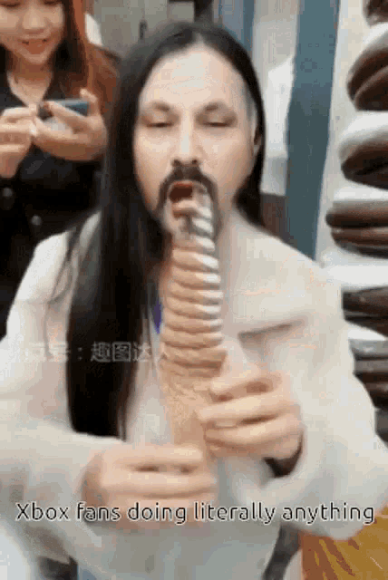 a man with long hair and a beard is eating an ice cream cone with the words xbox fans doing literally anything .