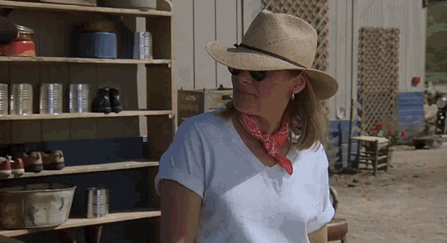 a woman wearing a straw hat and a bandana stands in front of a shelf