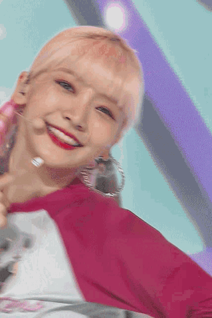 a girl with pink hair and hoop earrings smiles for the camera