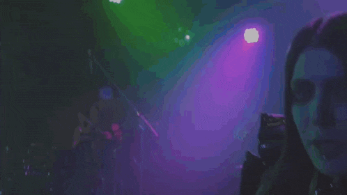 a woman is standing in front of a microphone in a dark room with purple lights behind her .