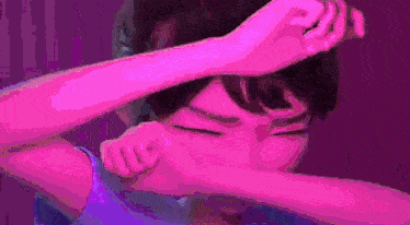 a person is covering their face with their hands in a purple background .