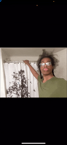 a person wearing glasses is holding a shower curtain in a bathroom