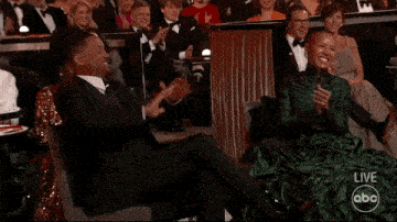 a man in a suit and a woman in a green dress are sitting in a crowd watching a live abc broadcast