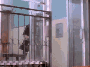 a person is standing on a balcony behind a fence with a bag on their shoulder .