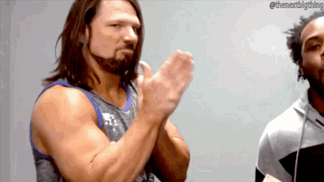a man with long hair and a beard is clapping his hands in front of another man .