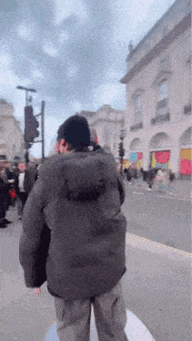 a man in a black jacket is walking down a street in front of a building