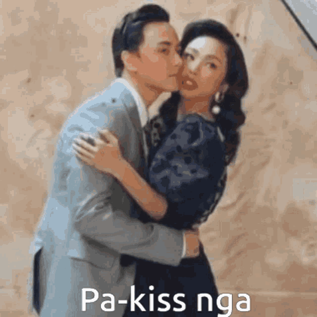 a man in a suit is kissing a woman on the cheek in front of a wall .