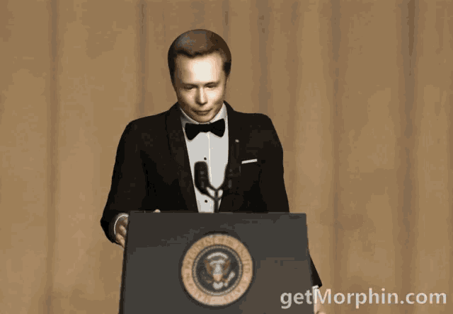 a man in a tuxedo stands behind a podium with the united states of america seal on it