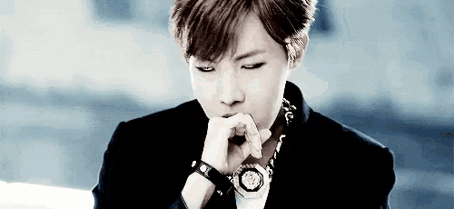 a close up of a person wearing a watch and a necklace with their hand on their chin .