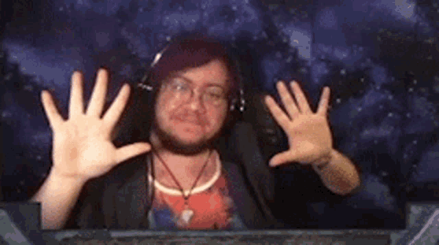 a man wearing headphones and glasses is making a funny face with his hands behind a glass .