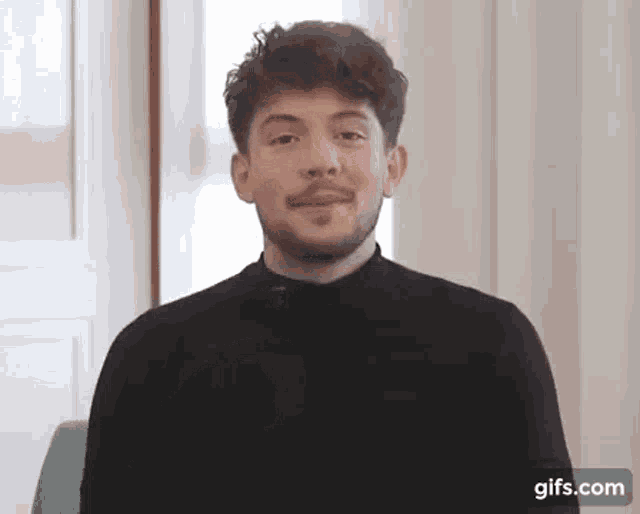 a young man with a beard is wearing a black turtleneck sweater and smiling .