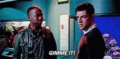 two men are standing next to each other in a room and one of them is saying gimme it !