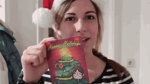 a woman wearing a santa hat is holding a christmas card that says happy holidays .