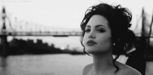 a black and white photo of a woman standing in front of a bridge .