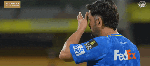a man wearing a blue fedex shirt wipes his face