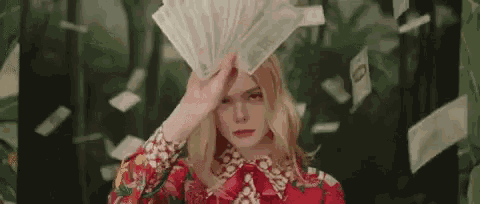 a woman is holding a fan of money over her face while money is falling around her .