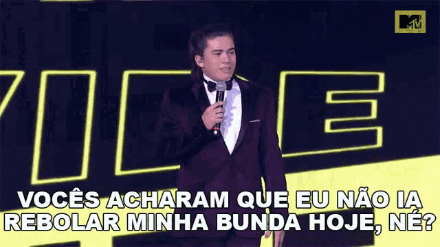 a man in a tuxedo holds a microphone in front of a sign that says voce