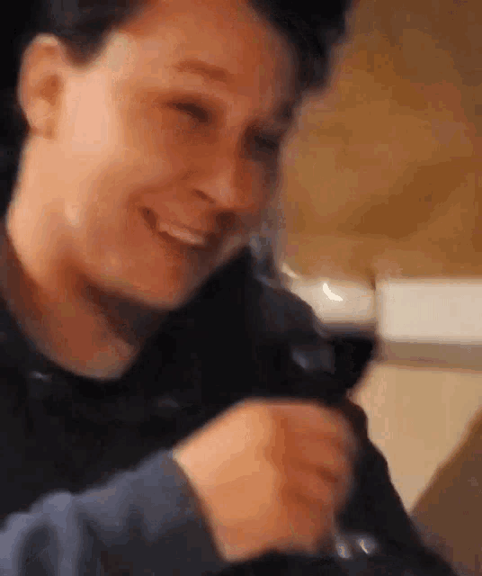 a man is drinking a glass of red wine and smiling .