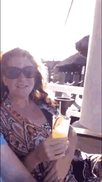 a woman wearing sunglasses is holding a drink in her hand .