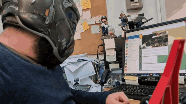 a man wearing a helmet sits in front of a computer monitor