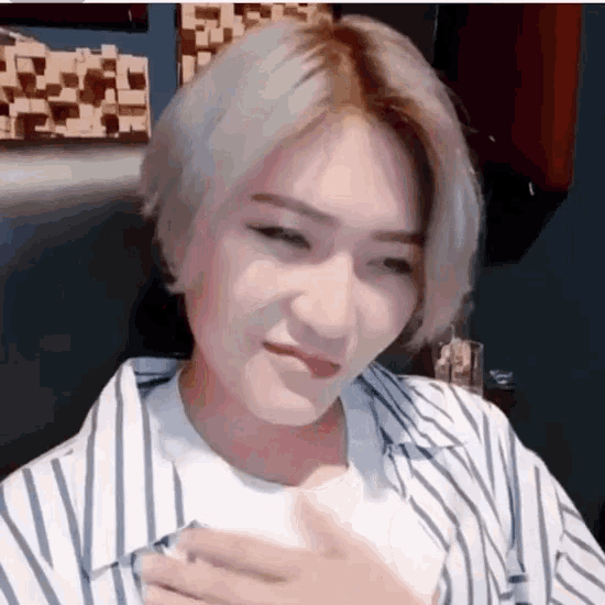 a woman with short blonde hair is wearing a striped shirt and holding her chest .