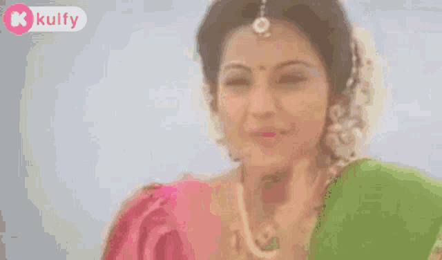 a close up of a woman in a green and pink saree smiling .