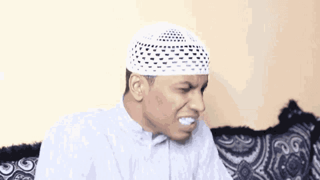 a man wearing a white hat and a white shirt is sitting on a couch .