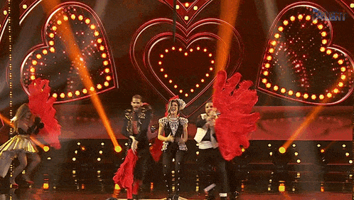 a group of people are dancing on a stage in front of a heart shaped sign