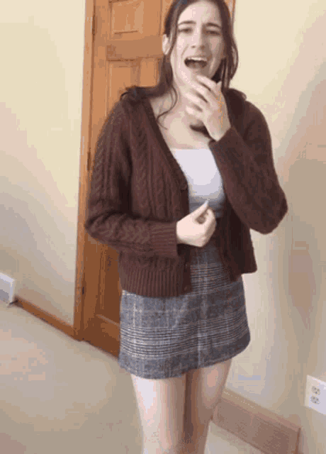 a woman wearing a brown cardigan and a plaid skirt laughs