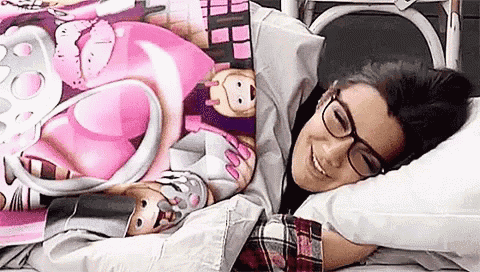 a woman wearing glasses is laying on a bed with a pink blanket and a pillow .