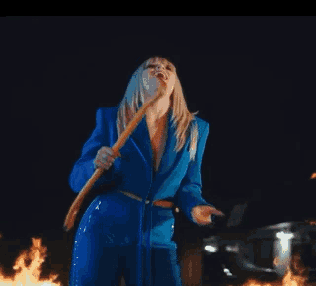 a woman in a blue suit is singing into a microphone while holding a guitar in front of a fire .