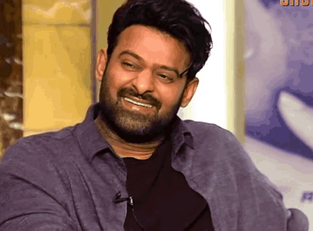 a man with a beard is smiling and wearing a purple shirt and black shirt .