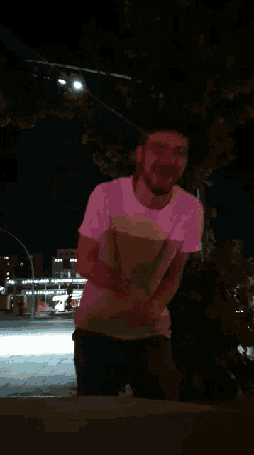a man in a purple shirt stands in front of a building at night