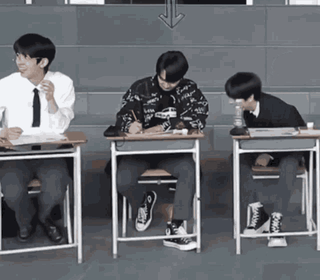 three boys are sitting at desks in a classroom with an arrow pointing to the right