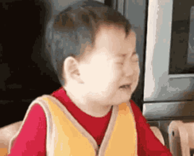 a baby is crying in front of a microwave while wearing a yellow vest .