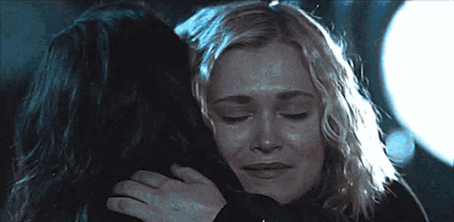 a woman is hugging another woman with her eyes closed in a dark room .