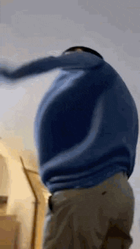 a man wearing a blue sweater and khaki pants is dancing in a room .