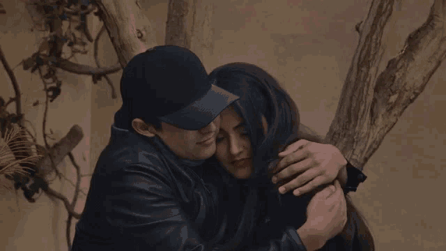 a man in a hat is hugging a woman in a black jacket .