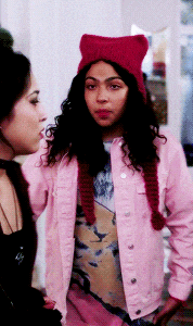 a woman wearing a pink jacket and a red hat talks to another woman