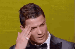 a man in a suit and bow tie is scratching his forehead with his hand .