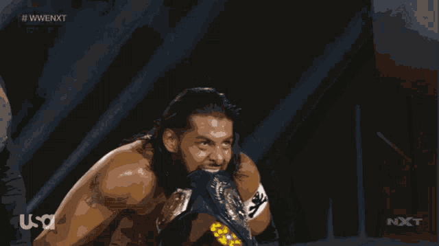a shirtless wrestler is holding a wrestling championship belt in front of a black background that says nxt