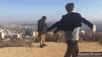 two men holding hands on top of a hill overlooking a city .